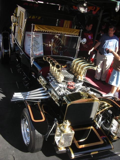 1998 Ford Crown Victoria - Front view of a black-and-gold T-bucket hot rod with chrome and brass velocity stacks and carriage lamps.
