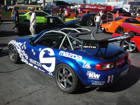 1998 Ford Crown Victoria - blue Mazda Miata roadster built as a race car with a roll cage, rear wing and Sparco and sponsor decals.