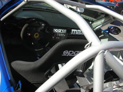 1998 Ford Crown Victoria - Interior of a blue Mazda race car showing a Sparco bucket seat, steering wheel and bare-metal roll cage.