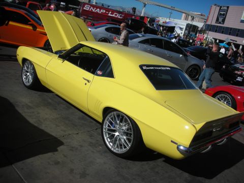 1998 Ford Crown Victoria - yellow first-generation Chevrolet Camaro restomod with billet wheels and a 'Power Tour' decal at an outdoor show.