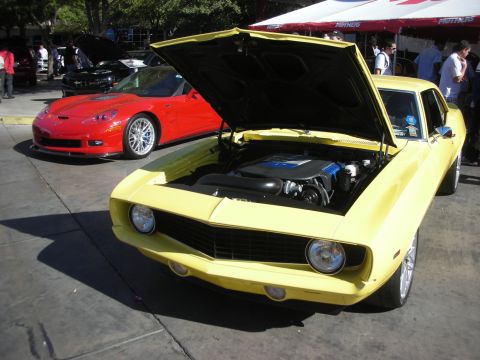 1998 Ford Crown Victoria - yellow classic muscle car displays its engine with hood raised next to a red sports car at an outdoor car show.