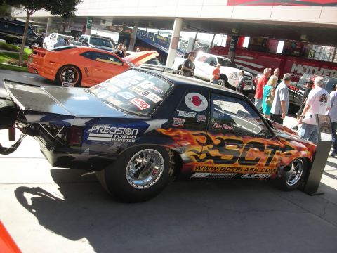 1998 Ford Crown Victoria - black turbocharged drag-style coupe with flame and SCT sponsor graphics sits on display amid show crowds.