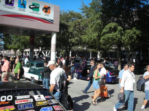 1998 Ford Crown Victoria - Crowds of attendees walk among display vehicles and sponsor banners at a large automotive trade expo.