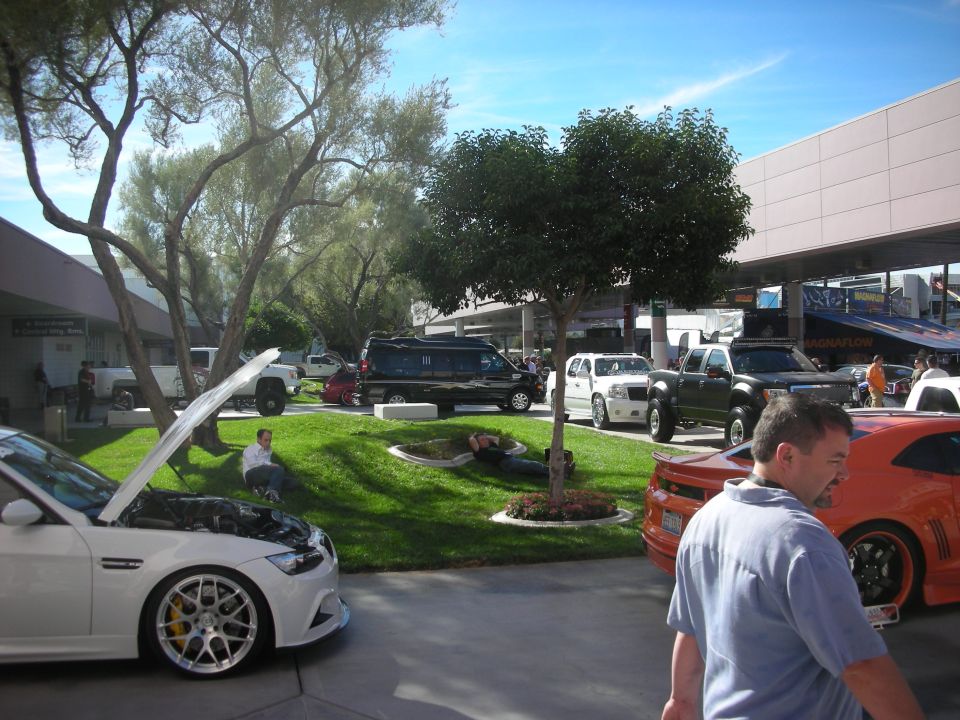 Auto expo courtyard with white car, trucks and people on grass