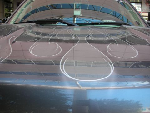 1998 Ford Crown Victoria - Detail of silver pinstripe flame artwork airbrushed across a glossy dark car body panel reflecting a building.