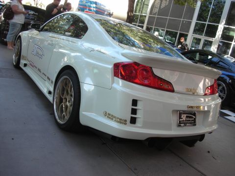 1998 Ford Crown Victoria - Rear three-quarter view of a white Infiniti-style coupe with widebody kit, spoiler and gold mesh wheels.