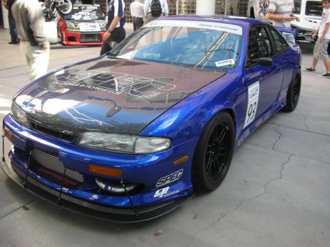 1998 Ford Crown Victoria - blue Nissan track coupe with carbon hood, front splitter and race number 93 parked on pavement at an expo.