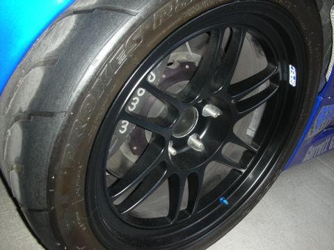 1998 Ford Crown Victoria - Close-up of a black multi-spoke racing wheel wrapped in a Toyo slick tire over a drilled brake rotor on a blue car.