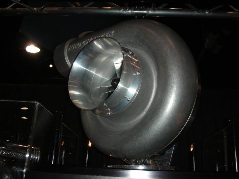 1998 Ford Crown Victoria - large polished centrifugal supercharger compressor mounted on a black display stand under spotlighting.