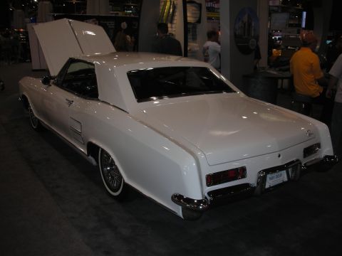 1998 Ford Crown Victoria - Rear three-quarter view of a white early-1960s Buick Riviera coupe with hood open on an indoor show stand.