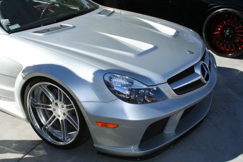 1998 Ford Crown Victoria - Detail of a silver Mercedes-Benz SL front corner with vented hood, projector headlight and a multi-spoke polished wheel.