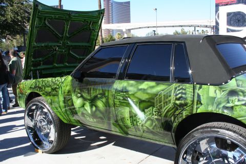 1998 Ford Crown Victoria - Profile of a custom car covered in green Hulk airbrush artwork riding on oversized chrome wheels with a black convertible top.