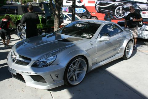 1998 Ford Crown Victoria - silver widebody Mercedes-Benz SL with Forgiato wheels and a for-sale sign parked at a sunny outdoor car show.