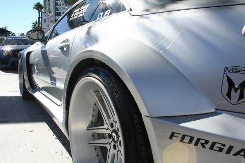 1998 Ford Crown Victoria - Closeup of a silver car's rear flare and polished wheel marked with Misha and Forgiato decals at an outdoor show.