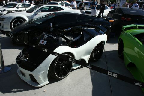 1998 Ford Crown Victoria - white-and-black custom Lamborghini Gallardo on black wheels behind a DUB rope barrier among other supercars.