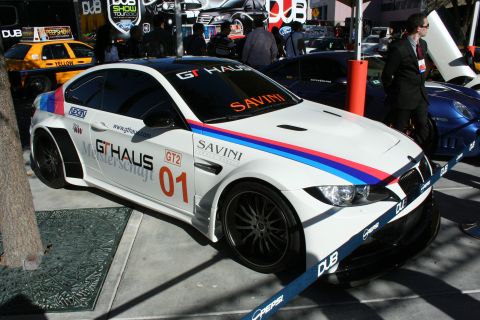 1998 Ford Crown Victoria - A customized white BMW M3, racing stripes and a wide body kit, is displayed at an event.