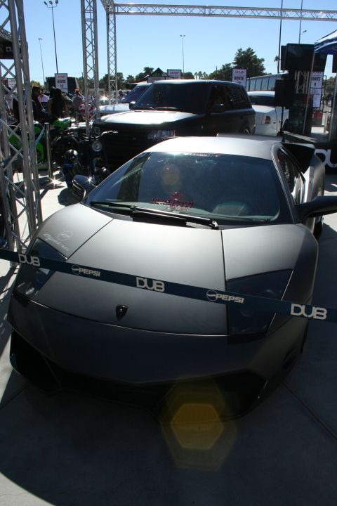 1998 Ford Crown Victoria - A matte gray Lamborghini Murcielago is displayed with promotional tape across its front.