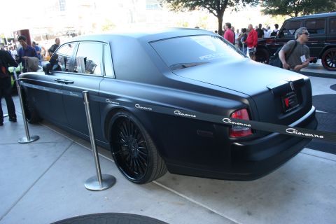1998 Ford Crown Victoria - Rear three-quarter view of a matte black Rolls-Royce Phantom sedan on black multi-spoke wheels with Giovanna decals.