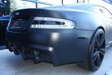 1998 Ford Crown Victoria - Rear-end detail of a matte black Aston Martin coupe with clear tail lights, rear diffuser and black wheels.