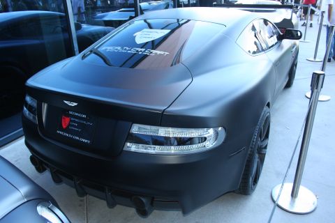 1998 Ford Crown Victoria - Rear three-quarter view of a matte black Aston Martin coupe with Specialty Car Craft decals and a quad exhaust.