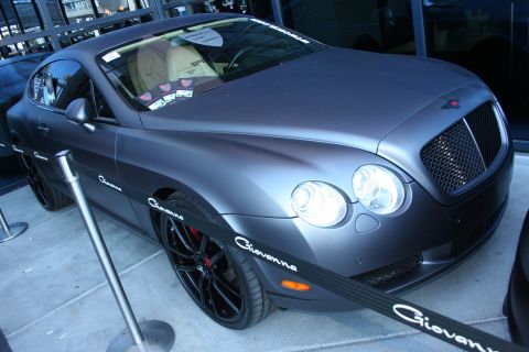 1998 Ford Crown Victoria - Matte gray Bentley Continental GT coupe on black wheels with red brake calipers and Giovanna decals at an outdoor show.