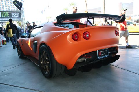 1998 Ford Crown Victoria - Rear view of an orange Lotus convertible with a large rear wing and twin tail lights at a busy street event.