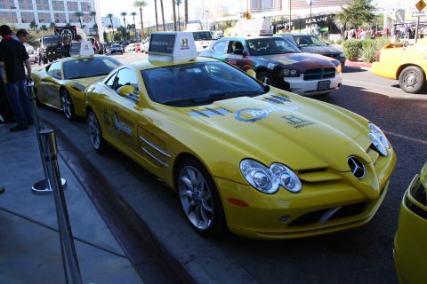 1998 Ford Crown Victoria - Yellow Mercedes-Benz SLR McLaren with a roof sign parked in a row of yellow promotional cars on a city street.