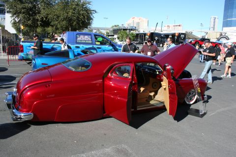 1998 Ford Crown Victoria - Candy red custom lead-sled hot rod with chopped roof and open doors displayed in an outdoor show parking lot.