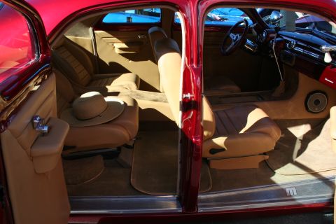 1998 Ford Crown Victoria - Tan leather interior of a candy red custom car seen through open doors, with a sun hat resting on the rear seat.