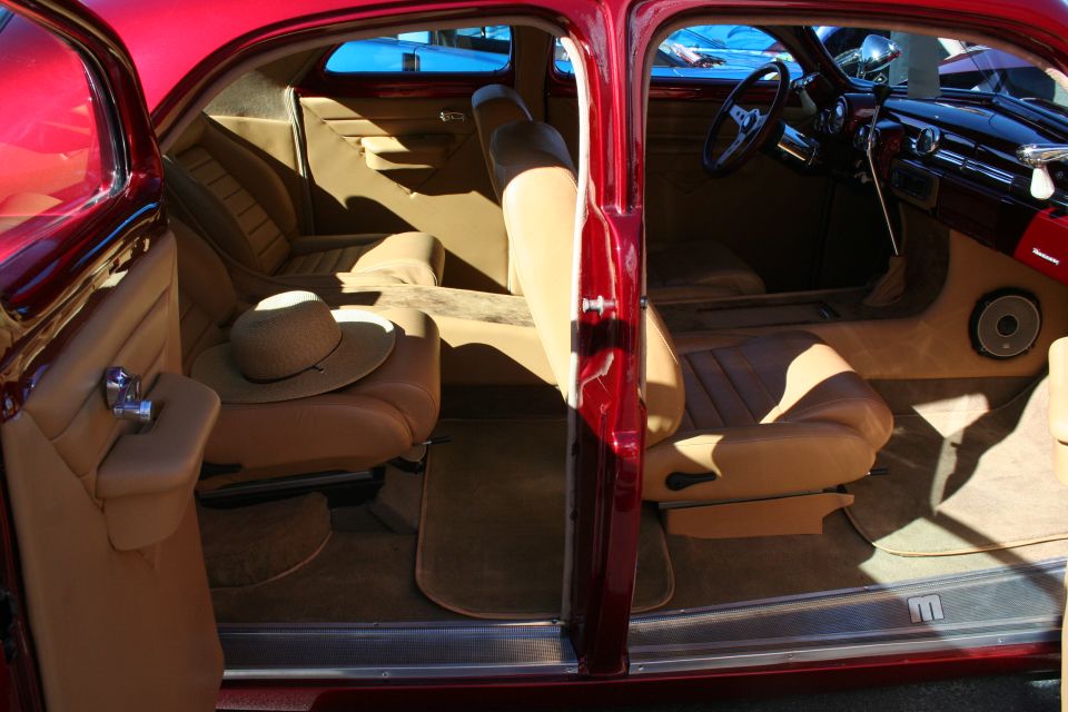 Tan leather interior of a candy red custom car viewed through open doors with a sun hat on the seat
