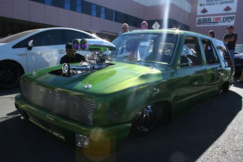 1998 Ford Crown Victoria - candy-green lowered mini-truck with a chromed supercharged engine protruding through the hood at a tire expo.