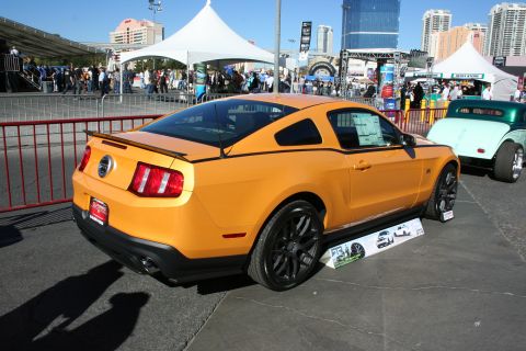 1998 Ford Crown Victoria - Rear three-quarter view of an orange Ford Mustang coupe on black wheels displayed at a crowded outdoor event.