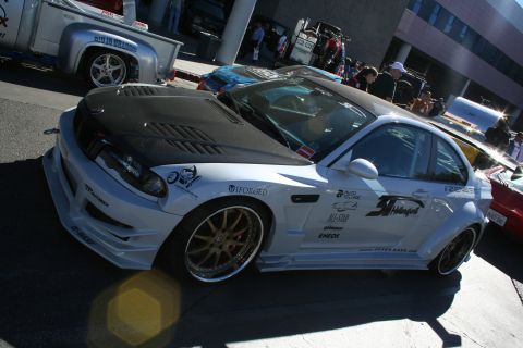 1998 Ford Crown Victoria - white widebody coupe with a vented carbon hood, heavy sponsor decals and bronze multi-spoke wheels at a show.