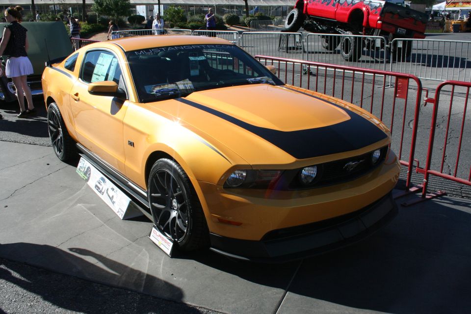 Orange Ford Mustang coupe with black hood stripe on black wheels