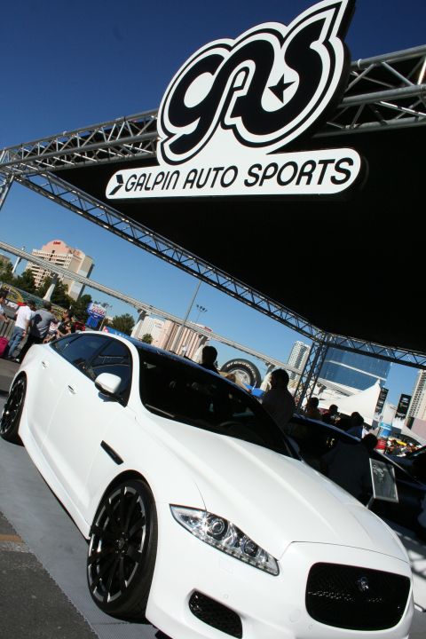 1998 Ford Crown Victoria - white Jaguar on black wheels sits beneath a large Galpin Auto Sports banner against a clear blue sky.