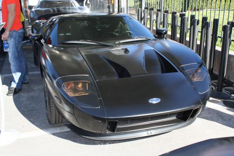 1998 Ford Crown Victoria - Front view of a matte-black Ford GT supercar with its distinctive low nose, parked behind black fencing.