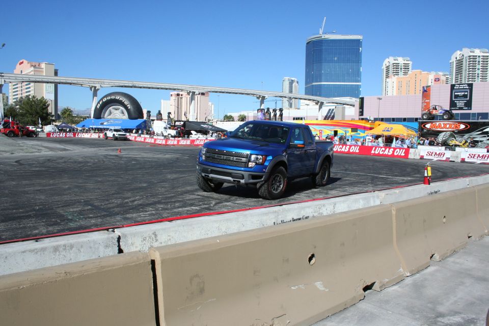 Blue Ford Raptor pickup driving on an outdoor course with Vegas skyline behind