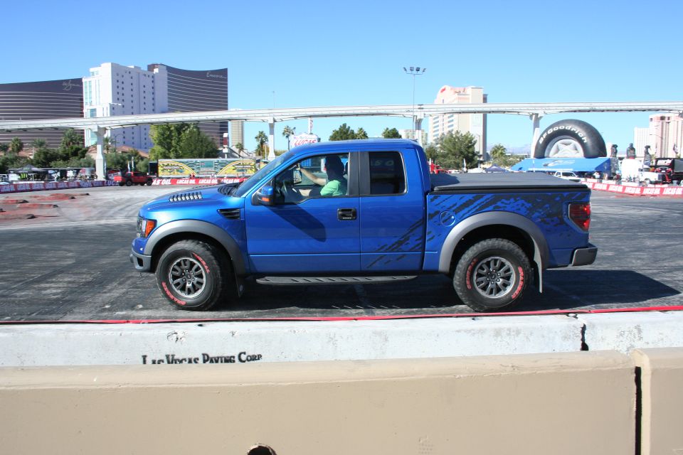Blue Ford Raptor pickup side profile parked on a paved demo course