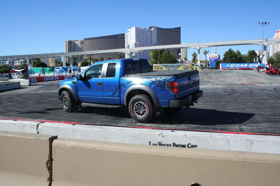 Blue Ford Raptor pickup rear three-quarter view on a demo course