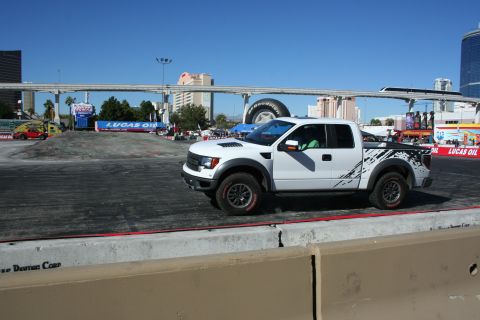 1998 Ford Crown Victoria - Front three-quarter view of a white Ford F-150 Raptor with splatter-style graphics on an asphalt course.