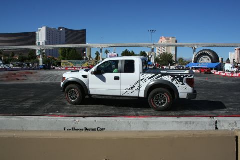 1998 Ford Crown Victoria - Side profile of a white Ford F-150 Raptor with black splatter graphics, parked on a paved demo course.