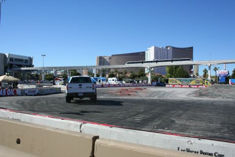 1998 Ford Crown Victoria - white pickup truck seen from behind on a paved demo course marked with tire skids, Vegas hotels in the distance.