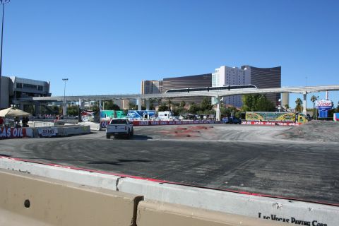 1998 Ford Crown Victoria - white pickup truck on a large paved demo course surrounded by Lucas Oil banners, with a monorail bridge and Vegas towers behind.