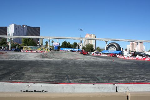 1998 Ford Crown Victoria - empty paved demo course ringed by Lucas Oil banners, with a large tire display and Las Vegas hotels in the background.