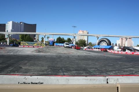 1998 Ford Crown Victoria - wide paved demo course with banners, a giant tire display and a distant white truck, with Las Vegas towers behind.