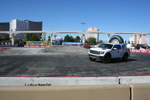 1998 Ford Crown Victoria - white Ford Raptor pickup sits on a graded dirt course ringed with Lucas Oil banners, the Las Vegas Strip skyline and monorail in the backgr…
