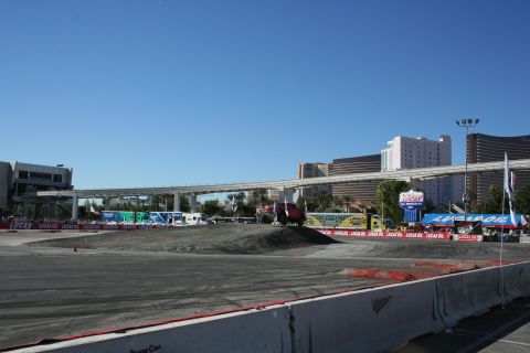 1998 Ford Crown Victoria - red truck sits at the edge of a graded dirt course ringed with Lucas Oil banners, Las Vegas casino towers and a monorail behind.