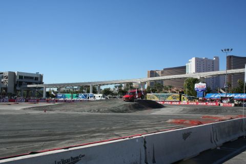 1998 Ford Crown Victoria - graded dirt course bordered by Lucas Oil banners with a red van parked at the rim and Las Vegas casino towers in the distance.
