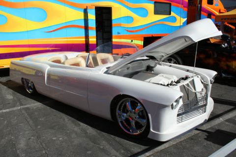 1998 Ford Crown Victoria - white custom convertible with chrome wheels and tan interior sits with its hood open beside a flame-painted trailer at an outdoor show.