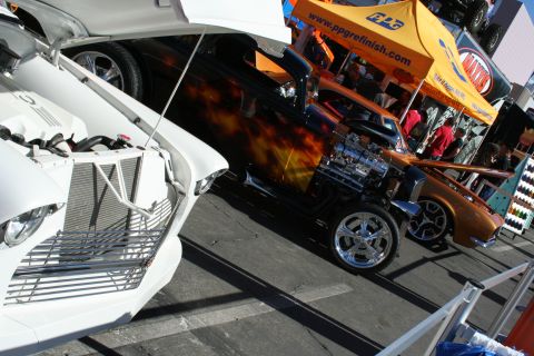 1998 Ford Crown Victoria - black hot rod with flame paint shows off a chromed V8 engine next to a white car and copper coupe at a PPG-sponsored show booth.